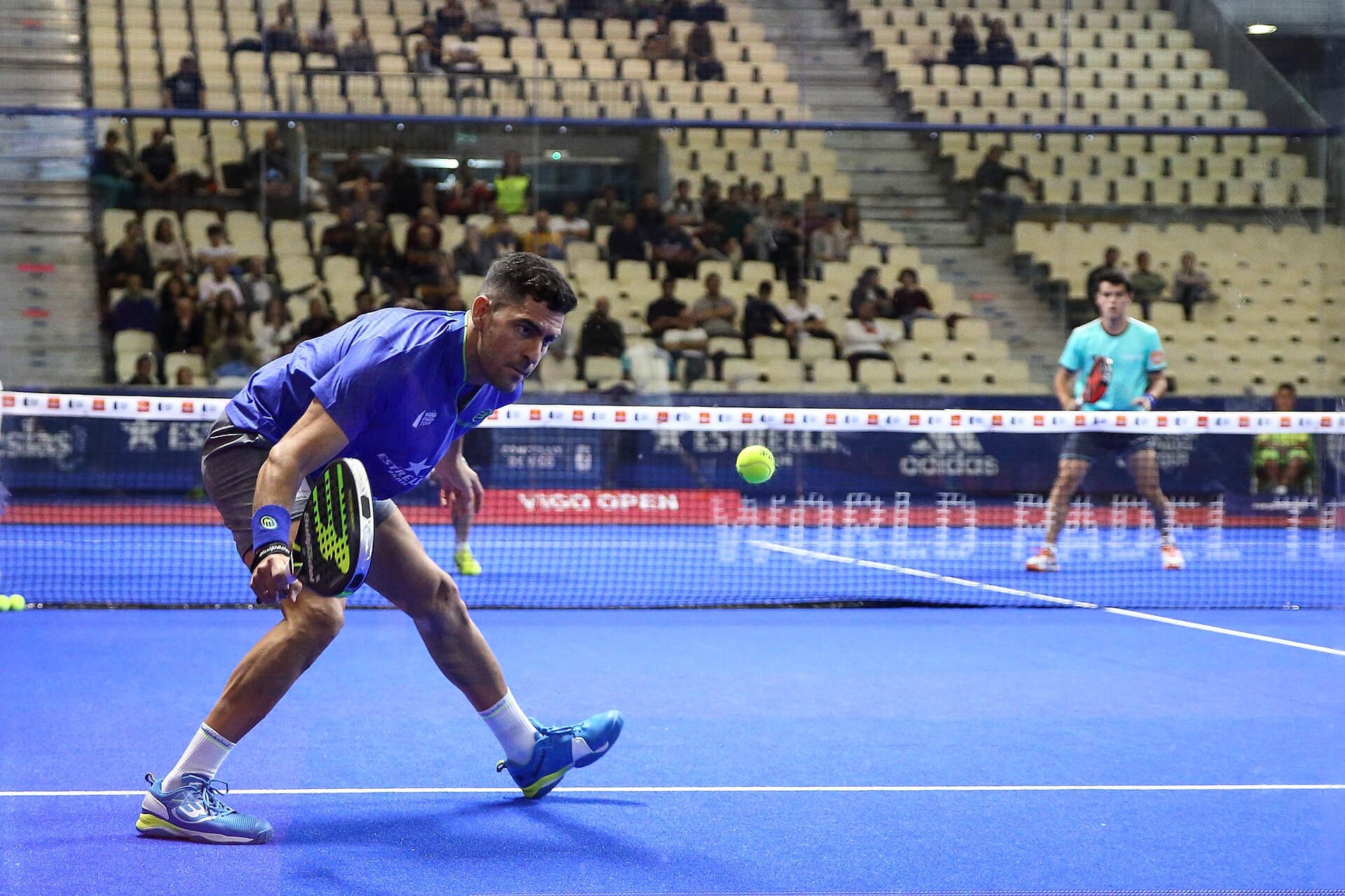 Jugador de pádel devolviendo una pelota baja en una cancha azul
